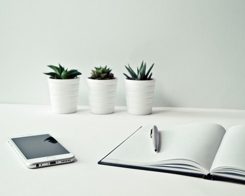 A clean, organized desk with a notebook, pen, and glass of water under warm daylight